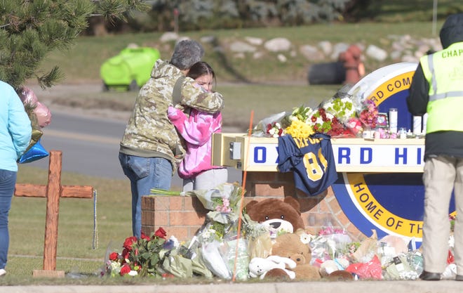 A parent hugs his daughter at a memorial at the entrance to Oxford High School on Thursday, Dec. 2, 2021. Four students were killed and seven others, including a teacher, were injured when sophomore Ethan Crumbley, 15, allegedly opened fire inside with a pistol in the school.