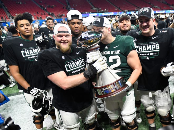 Michigan State’s Luke Campbell kisses the trophy he and his teammate pose for pictures after the Peach Bowl victory over Pitts.